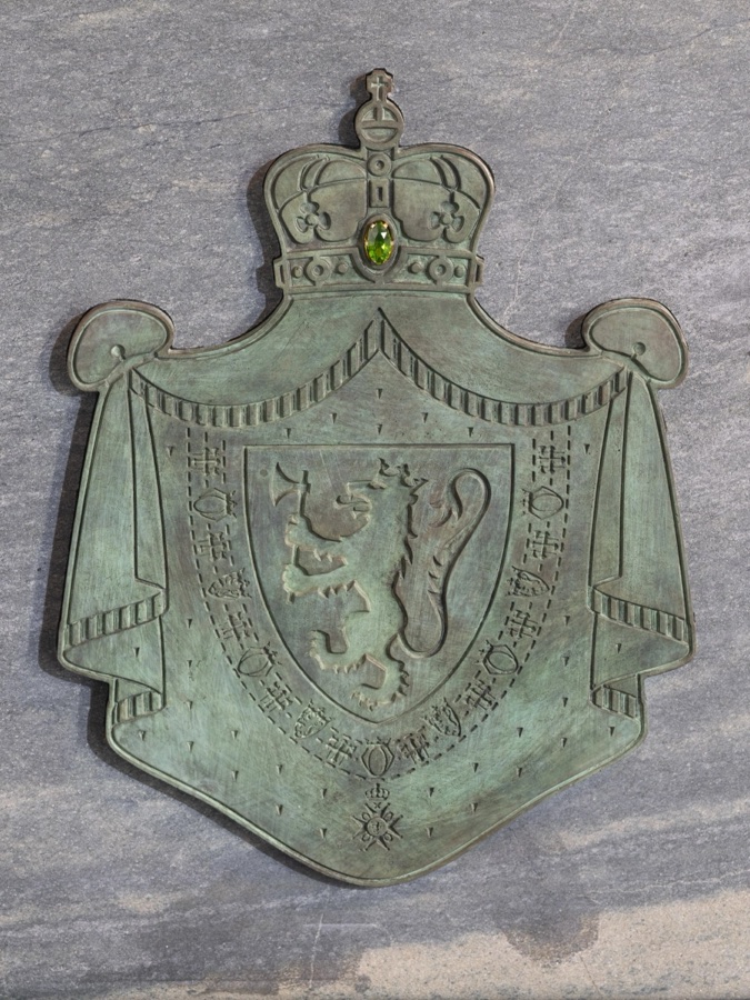 The royal coat of arms in bronze with a lion and crown, partly recessed into the grey-green stone