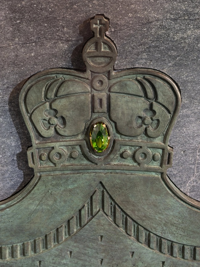 Close-up of a large green gemstone set in the middle of a bronze crown