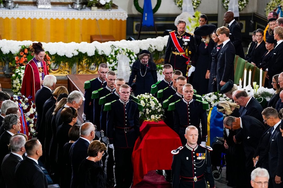 Guardsmen carry the coffin draped in the royal standard out of Oslo Cathedral, with King Haakon and foreign royals standing behind