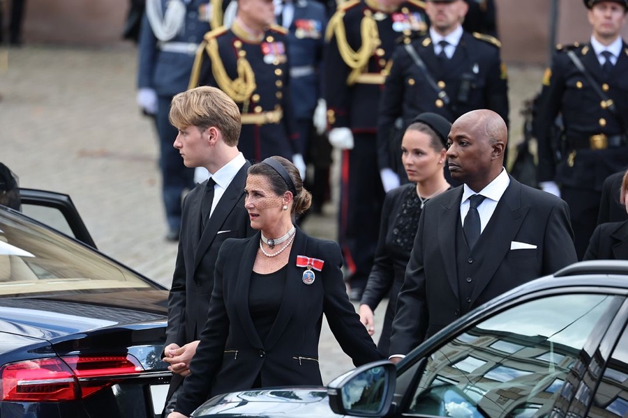 Prince Sverre Magnus, Princess Märtha Louise in a mourning veil and Durek Verrett walk between cars outside the church