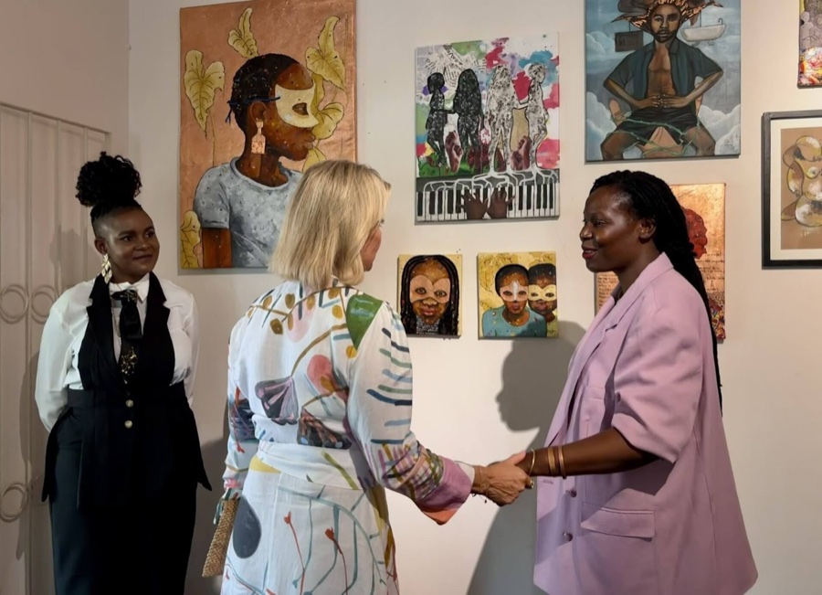 The Duchess of Edinburgh shakes hands with a woman in a light lilac blazer in front of a wall full of paintings