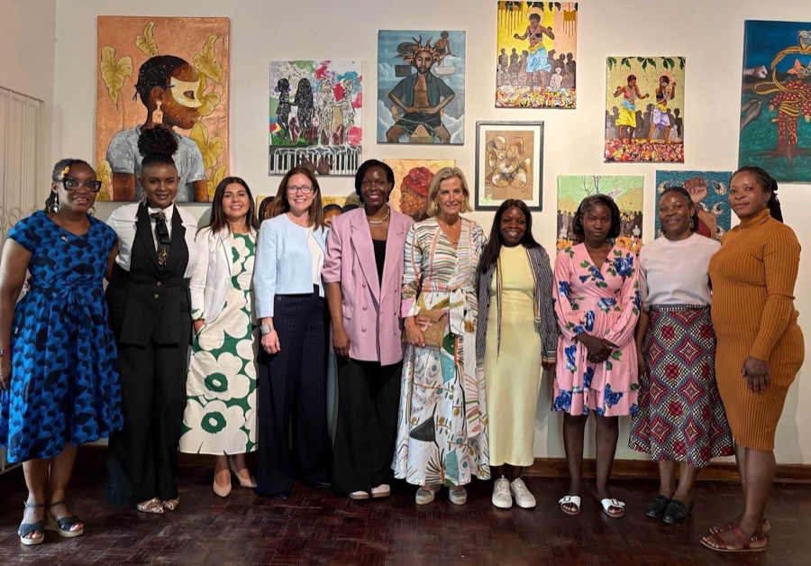 The Duchess of Edinburgh stands in the middle of a large group of women in front of a wall covered with colourful paintings