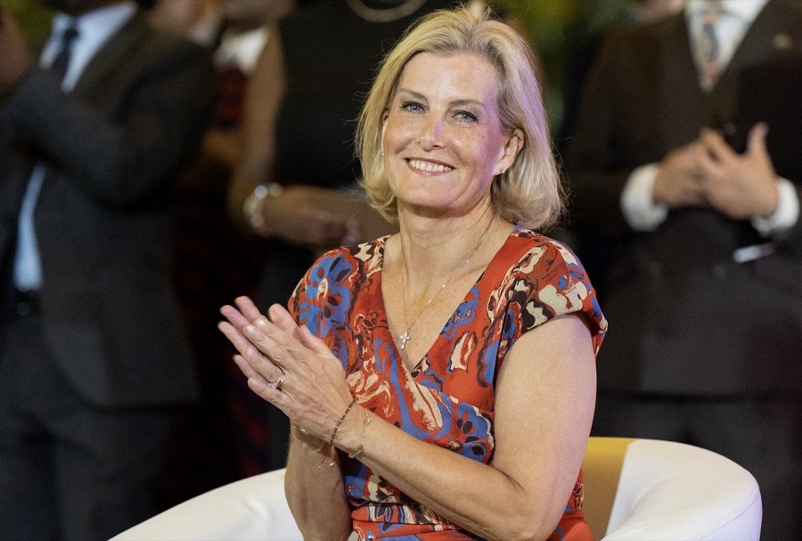 The Duchess of Edinburgh applauds and smiles while seated in a white armchair