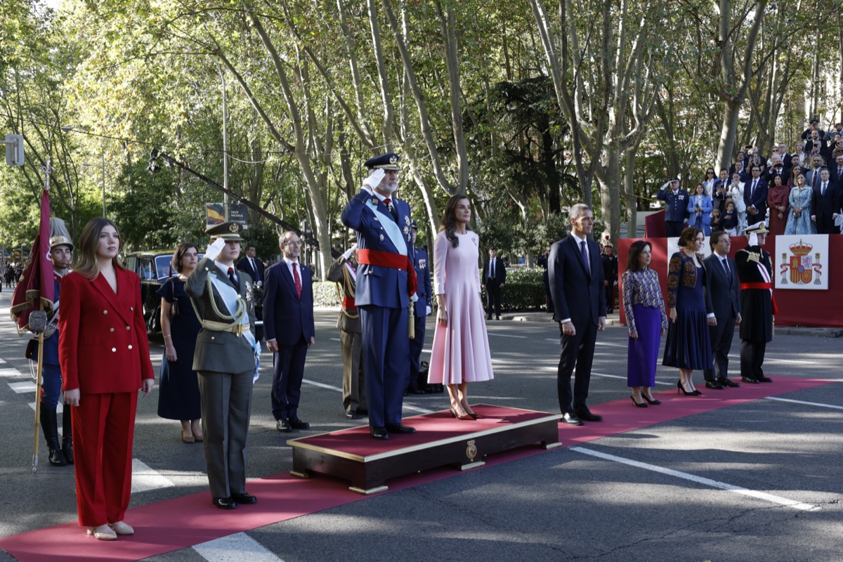 King Felipe salutes from the podium, with Queen Letizia beside him and Princess Leonor and Infanta Sofía in front