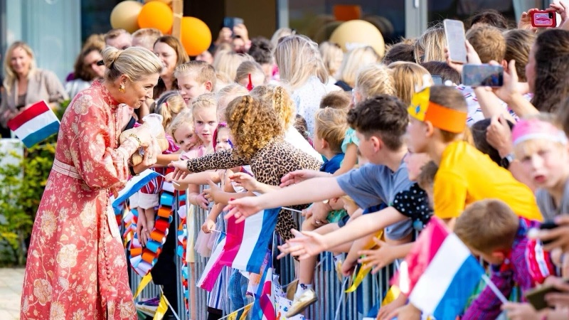 Dronning Máxima bøyer seg mot en lang rekke barn bak et gjerde, mange med flagg og tegninger