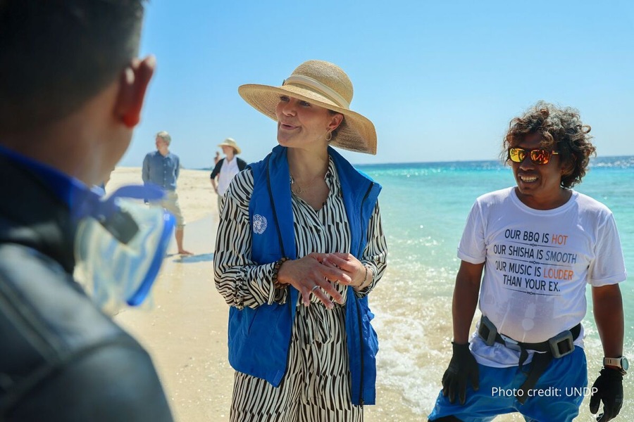 Crown Princess Victoria in a UNDP vest and straw hat stands on a beach on Lombok with local staff
