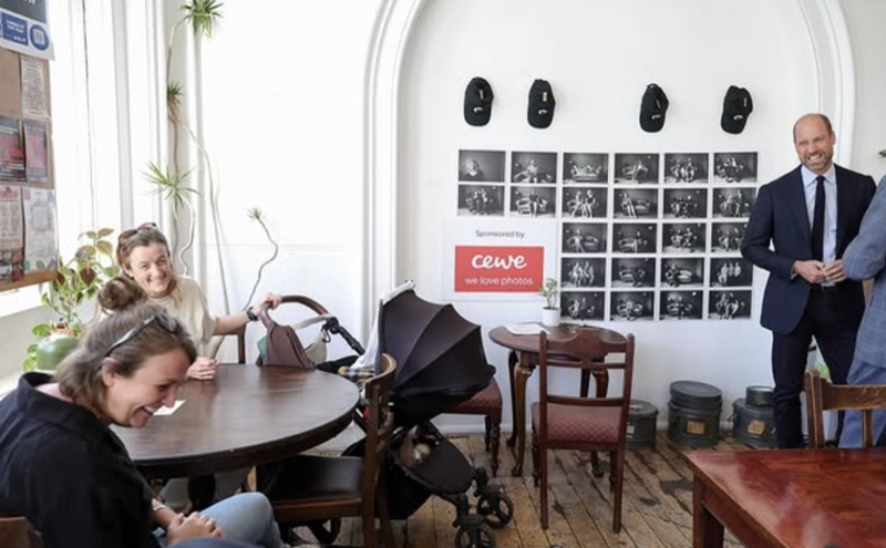 Prins William står ved en fotovegg i kinoens kafé mens gjester sitter rundt bordene