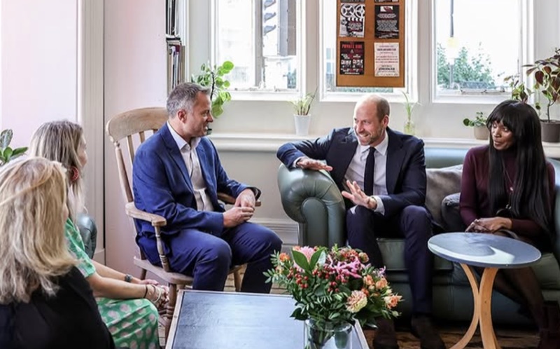 Prins William sitter i en sofa og samtaler med fire andre personer i et lyst rom med blomster på bordet