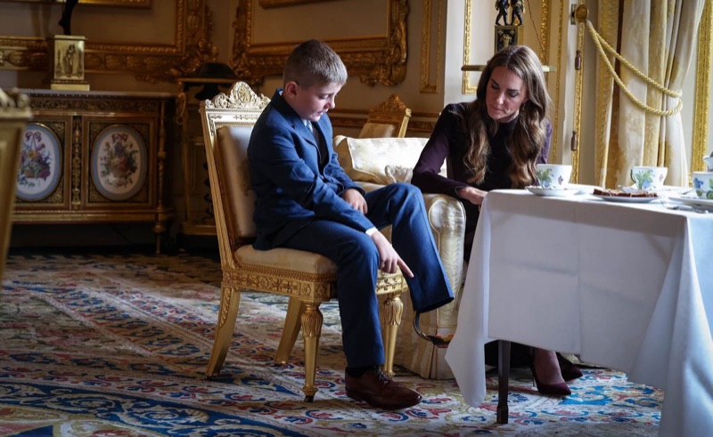 Prinsesse Catherine bøyer seg frem i samtale med en gutt i blå dress som sitter på en forgylt stol